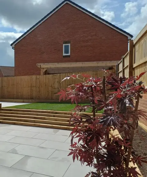 Finished garden with grey porcelain patio, timber sleeper steps up to a new lawn and a red acer