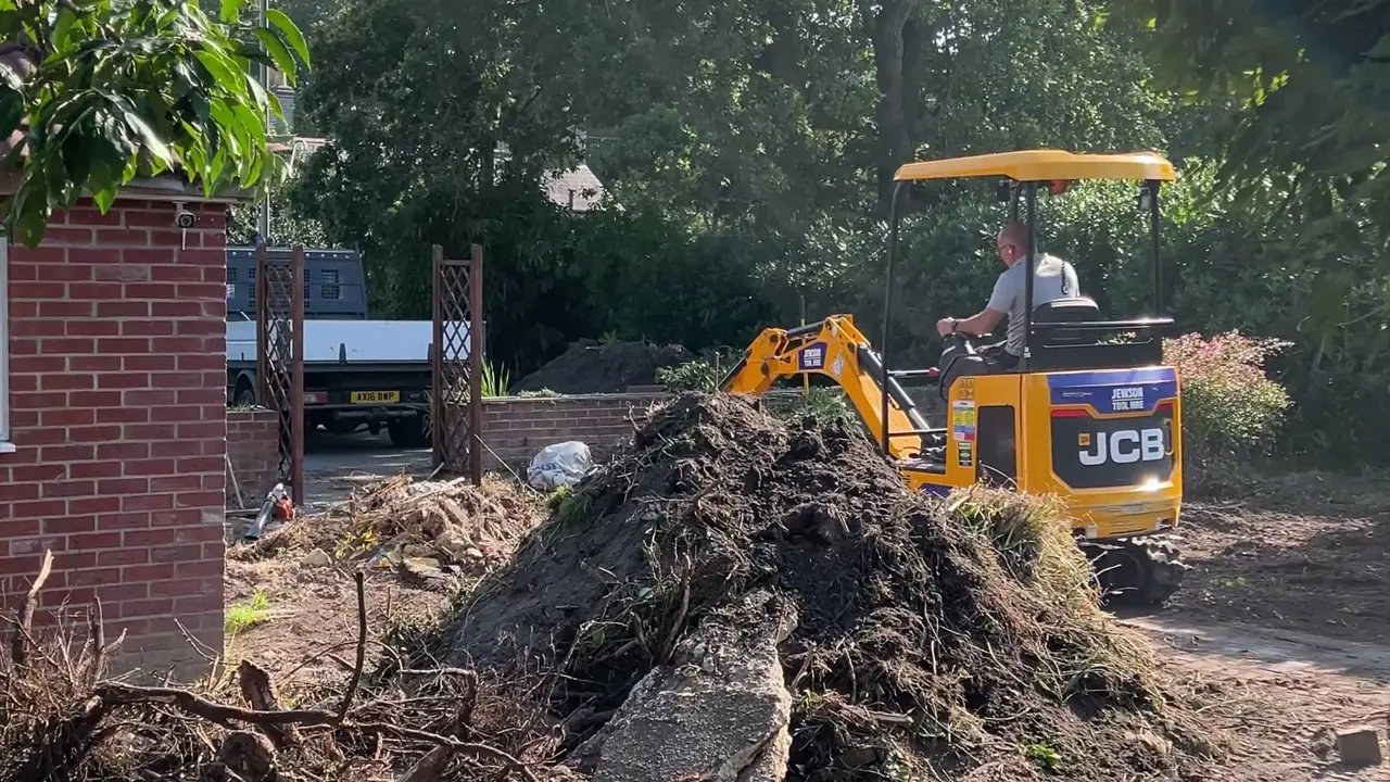 A mini digger at work behind a pile of cleared soil on a garden site