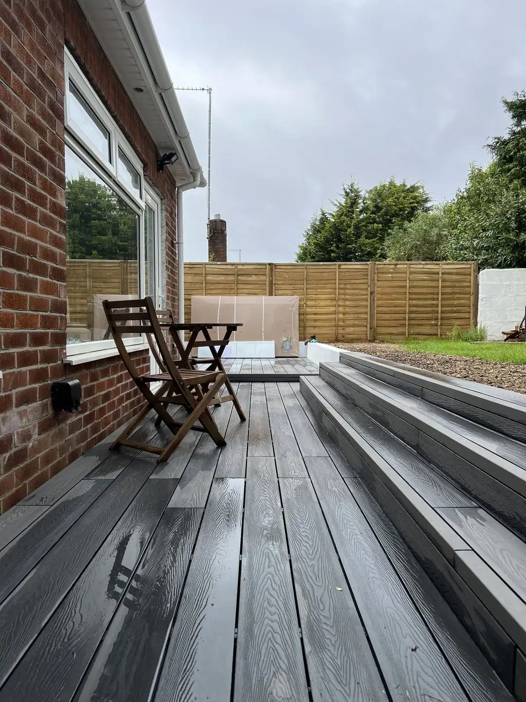 New grey composite decking with steps, beside a brick bungalow
